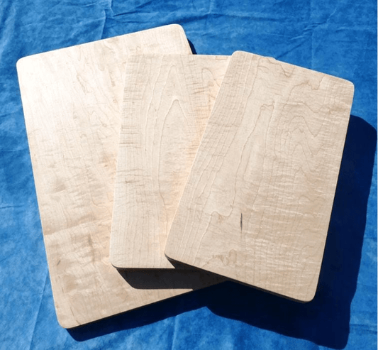 3 curly hard maple cutting boards with a blue background stacked over each other