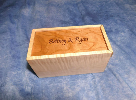 A soft curly maple wood box with an engraved curly cherry sliding lid and a curly walnut bottom sitting on a blue background