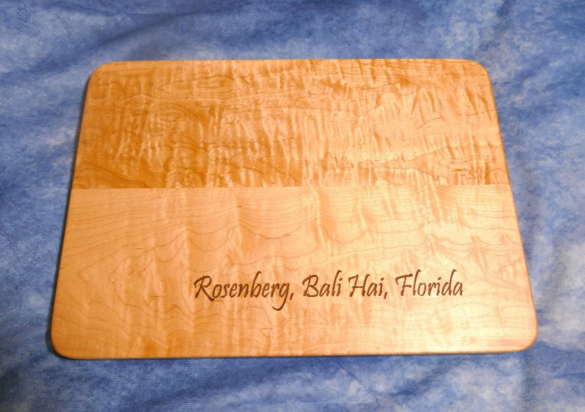 personalized, engraved, wooden cutting board made from hard curly maple hardwood on a blue background