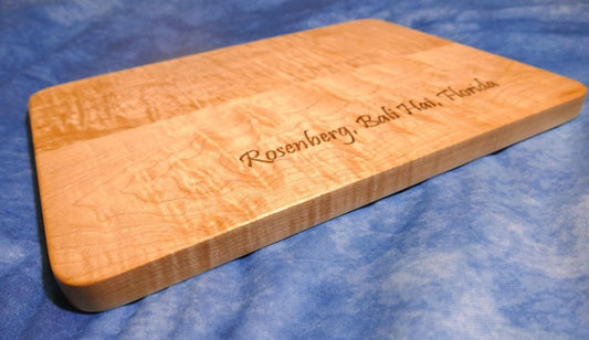 personalized, engraved, wooden cutting board made from hard curly maple hardwood on a blue background