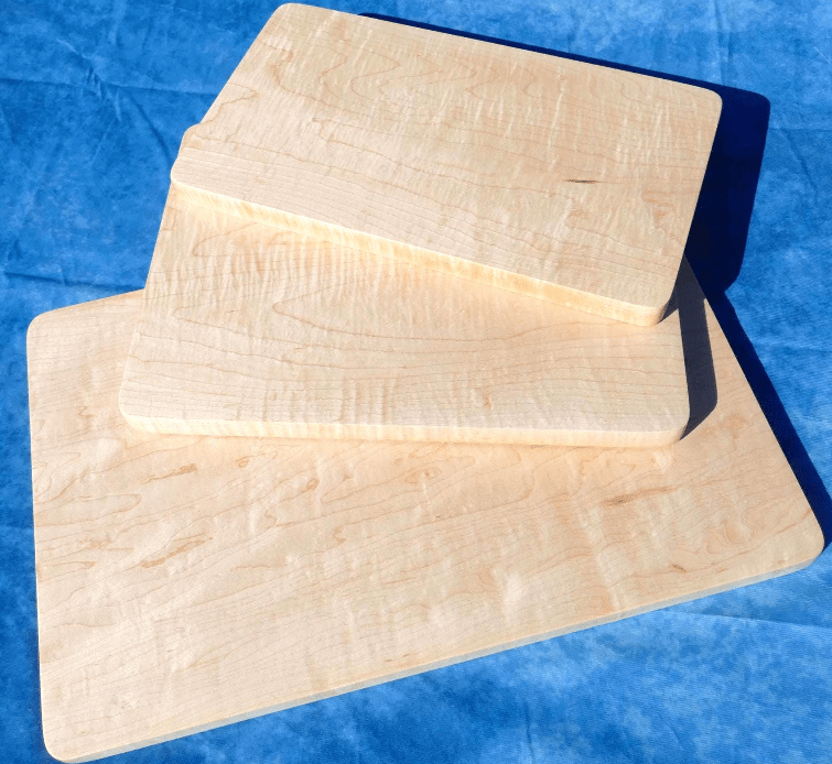 3 curly hard maple cutting boards with a blue background stacked over each other