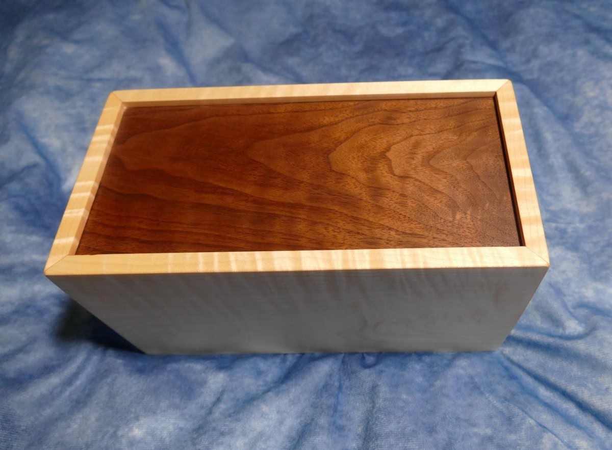 Bottom of the wooden box facing upward showing the curly walnut bottom of the box and the curly soft maple sides of the box