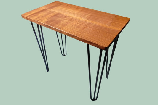 A figured black walnut tabletop with hairpin legs on top of a green background