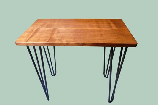 A figured black walnut tabletop with hairpin legs on top of a green background