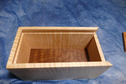 A soft curly maple wood box with the lid off showing the inside of the box surrounded by the blue background